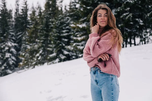 Ein junges, schönes, langhaariges Mädchen im rosa Pullover posiert in einem Winterwald in den Bergen — Stockfoto