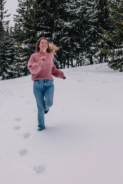 Młoda, szczupła, długowłosa dziewczyna biegnie przez śnieg w zimowym lesie w górach. — Zdjęcie stockowe