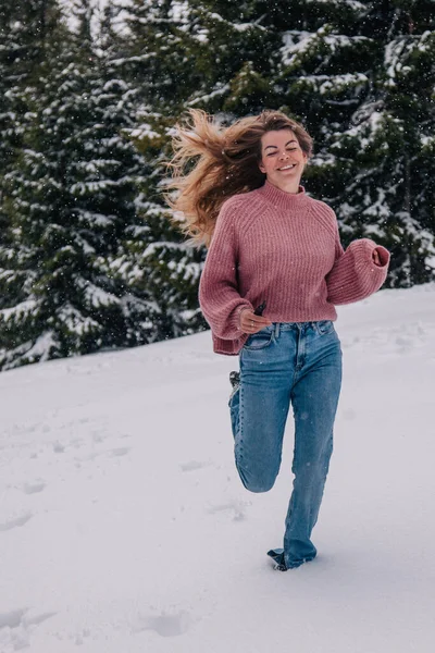 Genç, ince, uzun saçlı bir kız dağlardaki bir kış ormanında karda koşuyor.. — Stok fotoğraf