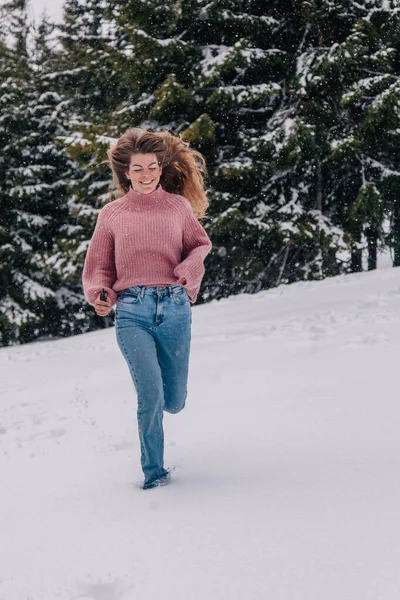 Mladá štíhlá, dlouhosrstá dívka běží sněhem v zimním lese v horách. — Stock fotografie