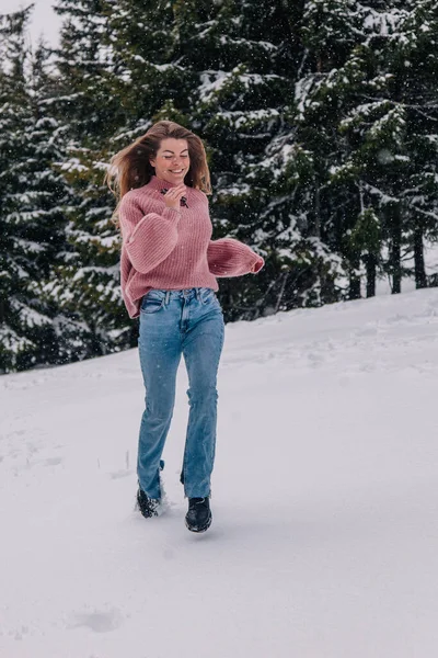 Una joven, delgada y de pelo largo corre por la nieve en un bosque de invierno en las montañas. — Foto de Stock