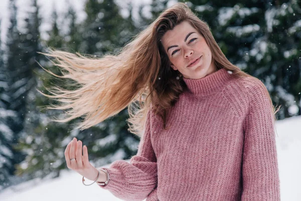 一个穿着粉色毛衣的年轻漂亮的长发姑娘在山里的一个冬季森林里摆姿势 — 图库照片