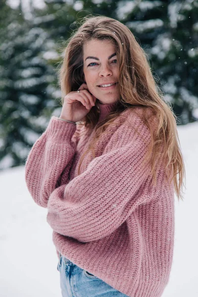 Une jeune, belle, aux cheveux longs dans un pull rose pose dans une forêt d'hiver dans les montagnes Image En Vente