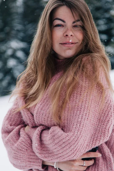 Une jeune, belle, aux cheveux longs dans un pull rose pose dans une forêt d'hiver dans les montagnes — Photo