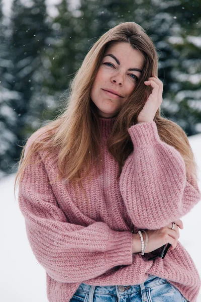Une jeune, belle, aux cheveux longs dans un pull rose pose dans une forêt d'hiver dans les montagnes — Photo
