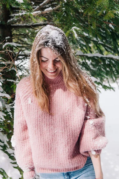 A young, cheerful girl sprinkled with snow under the branches of a spruce tree in the mountains — Stock Photo, Image