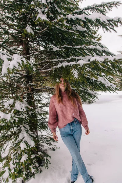 Uma jovem e alegre menina salpicada de neve sob os ramos de uma árvore de abeto nas montanhas — Fotografia de Stock