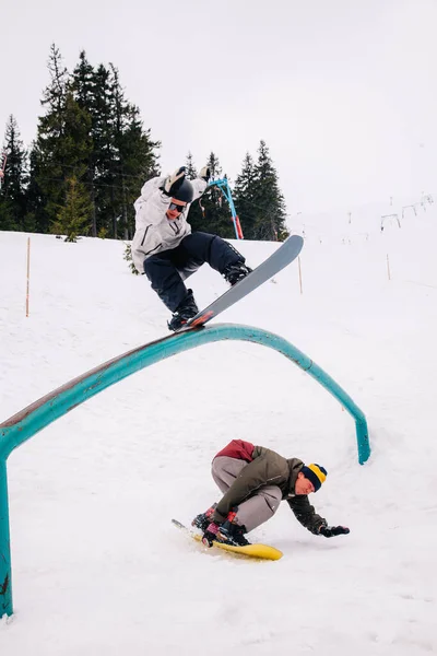 Snowboardista dělá trik na kolejích přes snowboardista závodní rychlostí — Stock fotografie