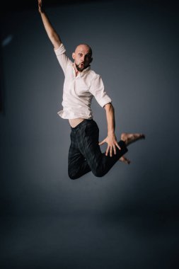 Beyaz gömlekli ve ekose pantolonlu, gri arka planda dans eden güzel sakallı, kel bir adamın stüdyo portresi.