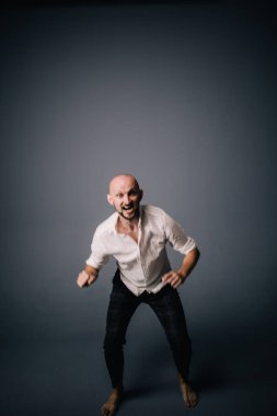 Beyaz gömlekli ve ekose pantolonlu, gri arka planda dans eden güzel sakallı, kel bir adamın stüdyo portresi.