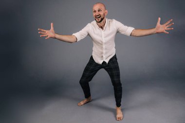 A bald guy in a white shirt and dark plaid pants throws up his hands on a gray background.