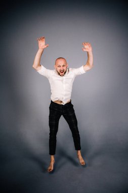 Beyaz gömlekli ve ekose pantolonlu, gri arka planda dans eden güzel sakallı, kel bir adamın stüdyo portresi.