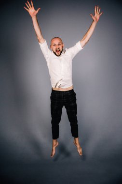 Beyaz gömlekli ve ekose pantolonlu, gri arka planda dans eden güzel sakallı, kel bir adamın stüdyo portresi.