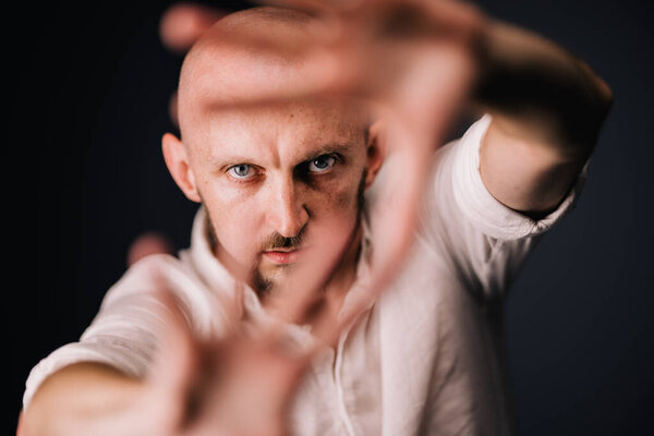 Studio portrait through the fingers of a bald man with a beautiful beard on a black background