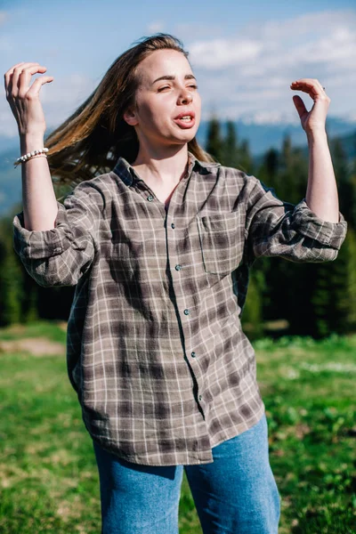 Une jeune fille mince avec les cheveux lâches dans une chemise à carreaux et un jean pose pour le temps ensoleillé dans les montagnes — Photo