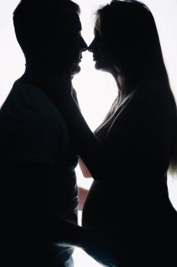 Tişörtlü bir adamın silueti ve beyaz arka planda güzel iç çamaşırlı hamile bir kadın. Stüdyo fotoğrafı. Yüksek kalite fotoğraf