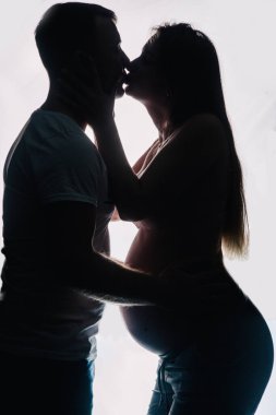 Tişörtlü bir adamın silueti ve beyaz arka planda güzel iç çamaşırlı hamile bir kadın. Stüdyo fotoğrafı. Yüksek kalite fotoğraf