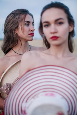 Bir tarlada birbirine aşık iki çıplak lezbiyen vücutlarını şapkalarla örtüyor. Yüksek kalite fotoğraf