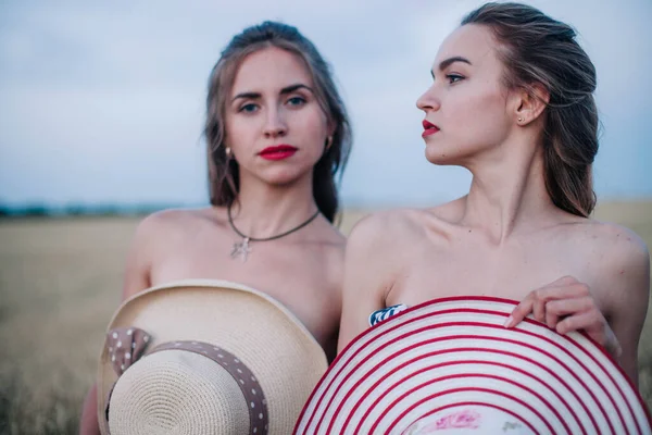 Bir tarlada birbirine aşık iki çıplak lezbiyen vücutlarını şapkalarla örtüyor. Yüksek kalite fotoğraf