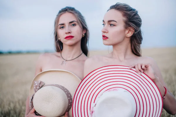 Bir tarlada birbirine aşık iki çıplak lezbiyen vücutlarını şapkalarla örtüyor. Yüksek kalite fotoğraf