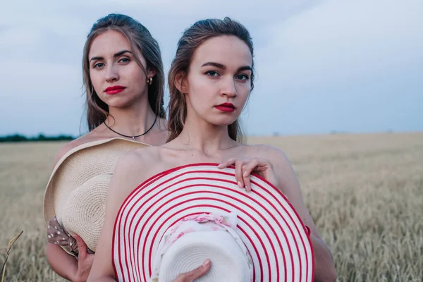 Bir tarlada birbirine aşık iki çıplak lezbiyen vücutlarını şapkalarla örtüyor. Yüksek kalite fotoğraf