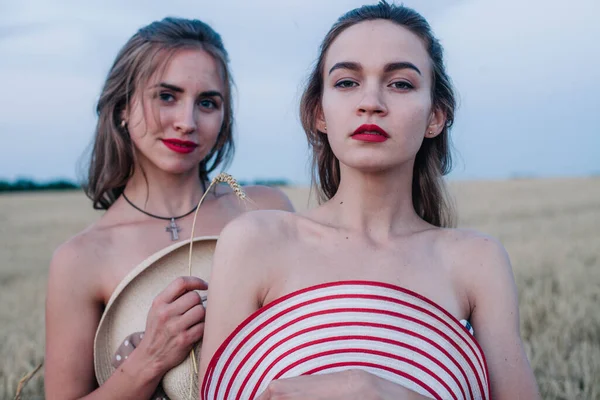 Bir tarlada birbirine aşık iki çıplak lezbiyen vücutlarını şapkalarla örtüyor. Yüksek kalite fotoğraf