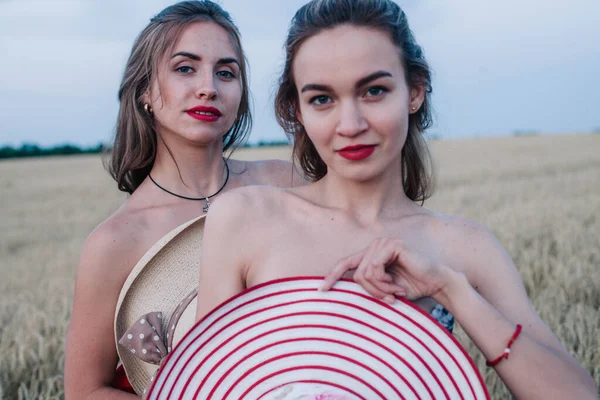 Bir tarlada birbirine aşık iki çıplak lezbiyen vücutlarını şapkalarla örtüyor. Yüksek kalite fotoğraf