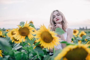 Tişörtü bol, ince saçlı genç bir kız gün batımında ayçiçeği tarlasında duruyor. Yüksek kalite fotoğraf