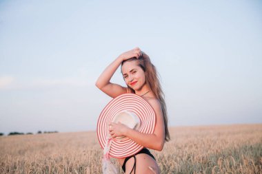 Buğday tarlasında siyah külotlu genç bir kadın göğsünü hasır bir şapkayla örtüyor. Yüksek kalite fotoğraf