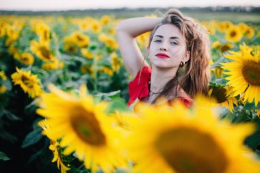 Gün batımında ayçiçeği tarlasında kırmızı elbiseli ve hasır şapkalı, gevşek saçlı, genç bir kız duruyor. Yüksek kalite fotoğraf