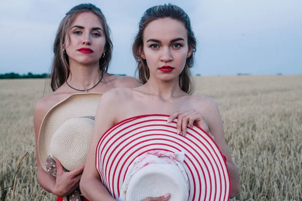 Bir tarlada birbirine aşık iki çıplak lezbiyen vücutlarını şapkalarla örtüyor. Yüksek kalite fotoğraf