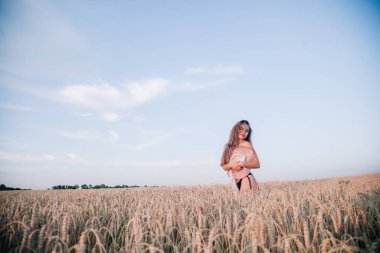Buğday tarlasında siyah külotlu genç bir kadın göğsünü hasır bir şapkayla örtüyor. Yüksek kalite fotoğraf