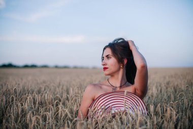 Buğday tarlasında siyah külotlu genç bir kadın göğsünü hasır bir şapkayla örtüyor. Yüksek kalite fotoğraf