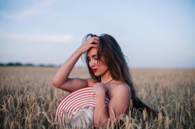 Buğday tarlasında siyah külotlu genç bir kadın göğsünü hasır bir şapkayla örtüyor. Yüksek kalite fotoğraf