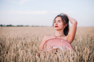 Buğday tarlasında siyah külotlu genç bir kadın göğsünü hasır bir şapkayla örtüyor. Yüksek kalite fotoğraf