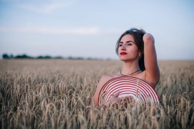 Buğday tarlasında siyah külotlu genç bir kadın göğsünü hasır bir şapkayla örtüyor. Yüksek kalite fotoğraf