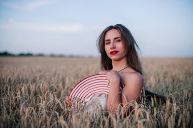 Buğday tarlasında siyah külotlu genç bir kadın göğsünü hasır bir şapkayla örtüyor. Yüksek kalite fotoğraf