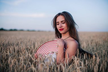 Buğday tarlasında siyah külotlu genç bir kadın göğsünü hasır bir şapkayla örtüyor. Yüksek kalite fotoğraf