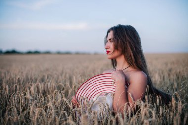 Buğday tarlasında siyah külotlu genç bir kadın göğsünü hasır bir şapkayla örtüyor. Yüksek kalite fotoğraf