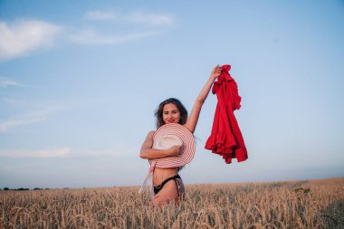 Buğday tarlasında elinde kırmızı bir elbiseyle siyah külotlu gevşek saçlı, genç bir kız. Yüksek kalite fotoğraf