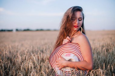 Buğday tarlasında siyah külotlu genç bir kadın göğsünü hasır bir şapkayla örtüyor. Yüksek kalite fotoğraf