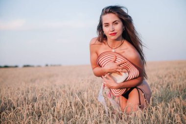 Buğday tarlasında siyah külotlu genç bir kadın göğsünü hasır bir şapkayla örtüyor. Yüksek kalite fotoğraf