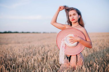 Buğday tarlasında siyah külotlu genç bir kadın göğsünü hasır bir şapkayla örtüyor. Yüksek kalite fotoğraf