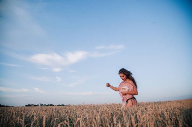 Buğday tarlasında siyah külotlu genç bir kadın göğsünü hasır bir şapkayla örtüyor. Yüksek kalite fotoğraf