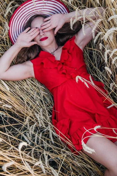 Młoda Smukła Seksowna Dziewczyna Jasnoczerwonej Sukience Kapeluszu Leży Polu Pszenicy — Zdjęcie stockowe