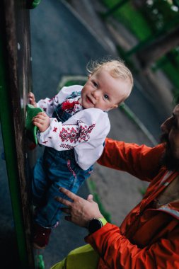 Baba, güneşli bir günde küçük kızıyla oyun parkında güzel bir Ukrayna gömleğiyle oynuyor. Yüksek kalite fotoğraf