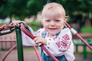 Parkta nakışlı gömlek ve kot tulumlu küçük bir kız oynuyor. Yüksek kalite fotoğraf