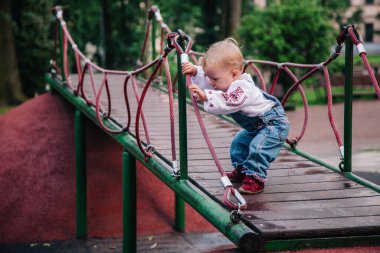 Parkta nakışlı gömlek ve kot tulumlu küçük bir kız oynuyor. Yüksek kalite fotoğraf