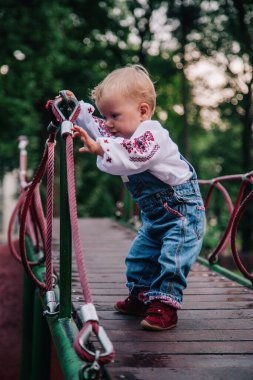 Parkta nakışlı gömlek ve kot tulumlu küçük bir kız oynuyor. Yüksek kalite fotoğraf