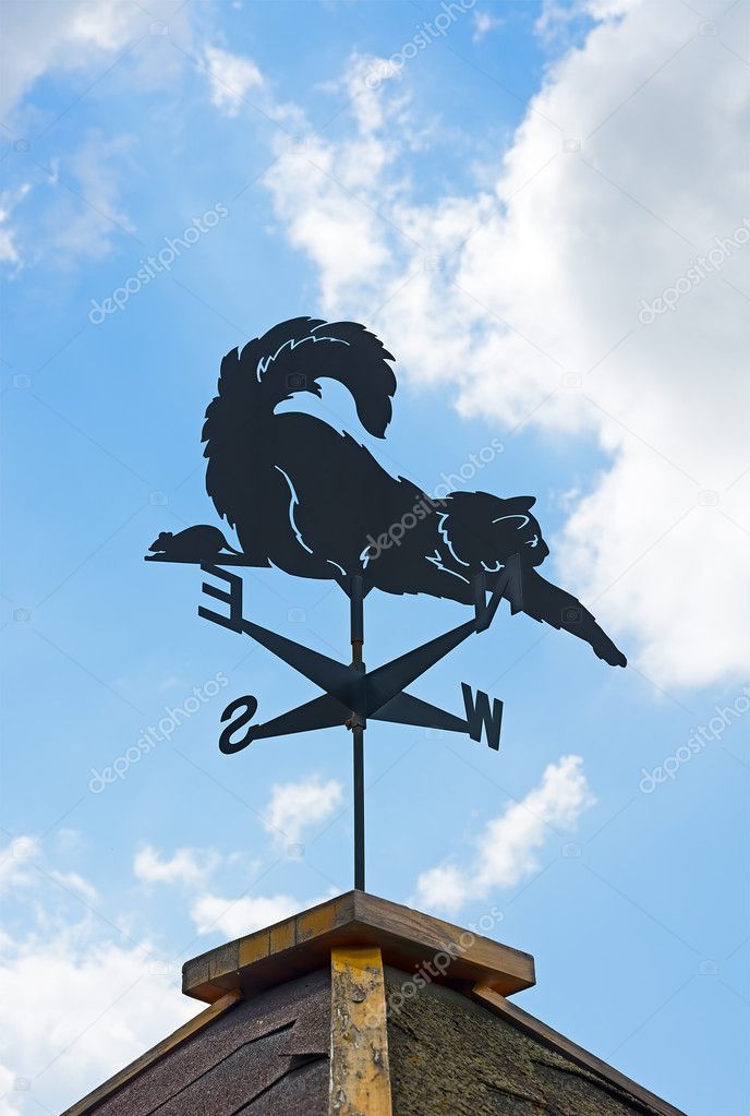 Weather vane on background of blue sky and clouds.